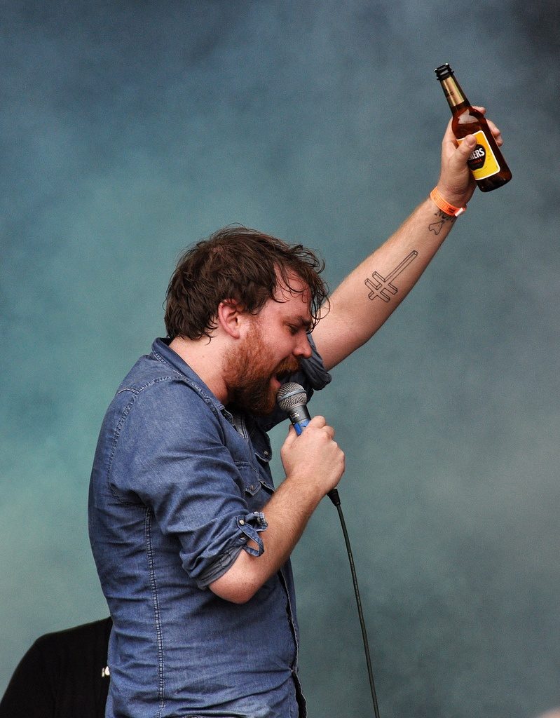 Scott Hutchison singing into a microphone, holding a bottle of beer